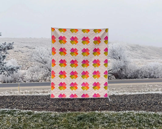 Colorful quilt with a geometric pattern displayed outdoors on a snowy landscape.